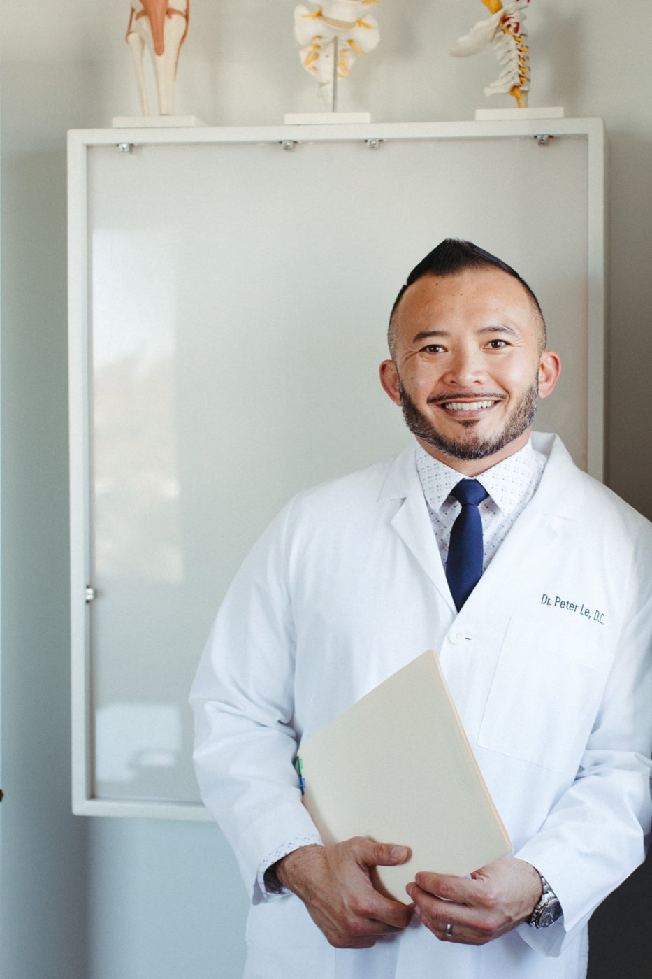 Dr. Peter Le, DC, in his white coat in front of spine models