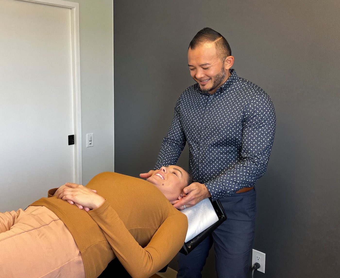 Dr. Peter Le giving gentle hands-on neck care to a smiling patient